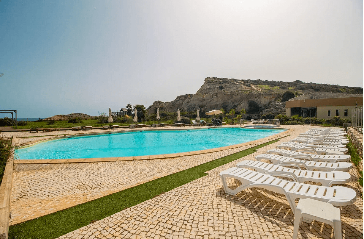 Sun loungers around the pool with cliffs behind.